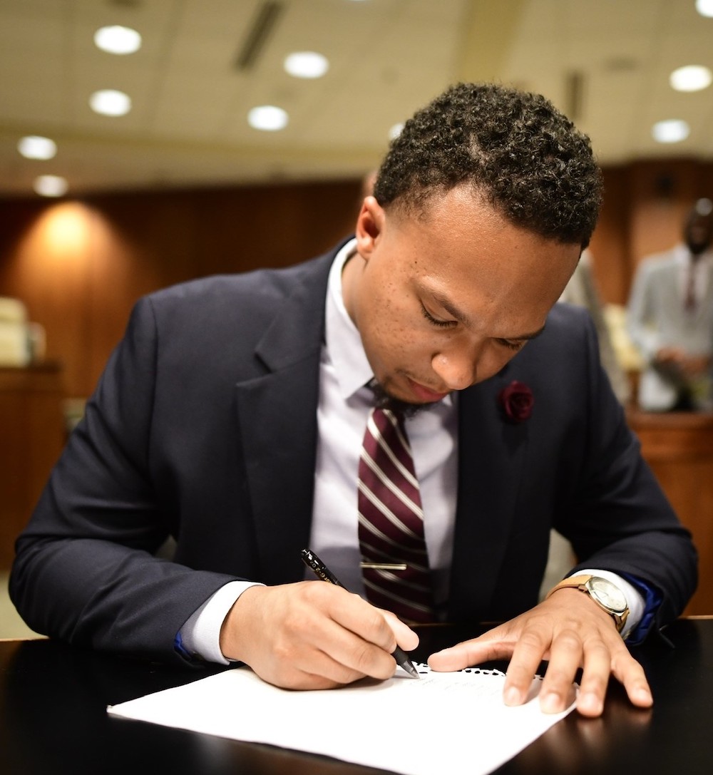 Young Black man in suit sitting at a table signing a paper