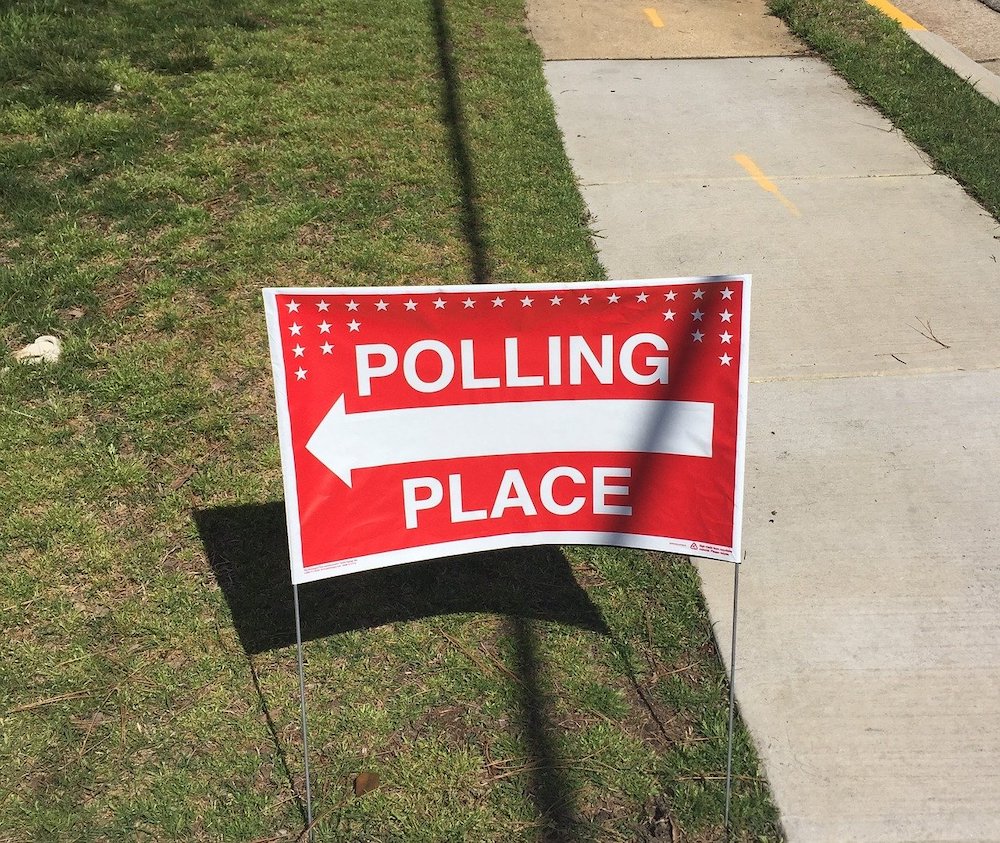 red "polling place" sign with arrow pointing left in grass next to a sidewalk.
