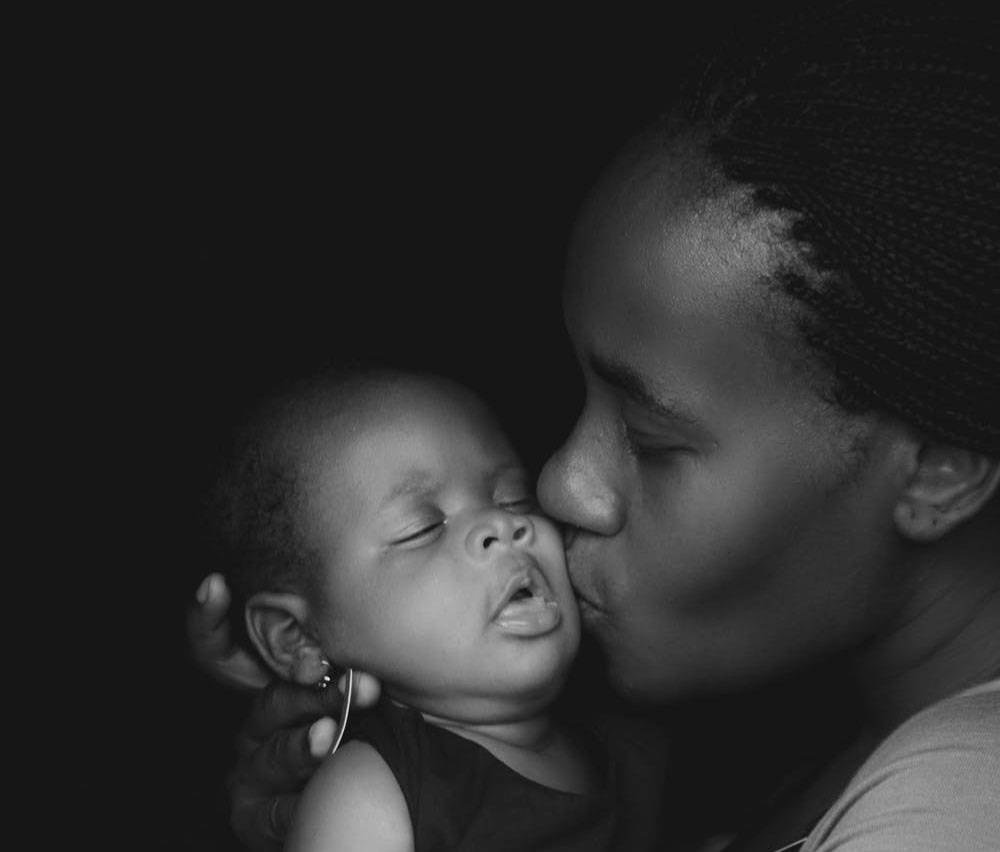black woman kissing newborn baby in her arms