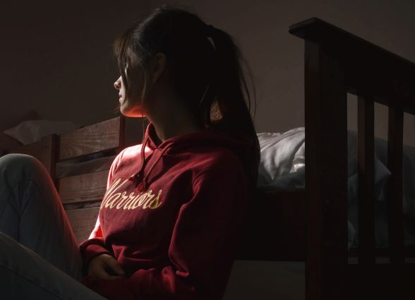 white girl with long black hair in pony wearing red sweatshirt sitting on the floor against her bed in a PRTF