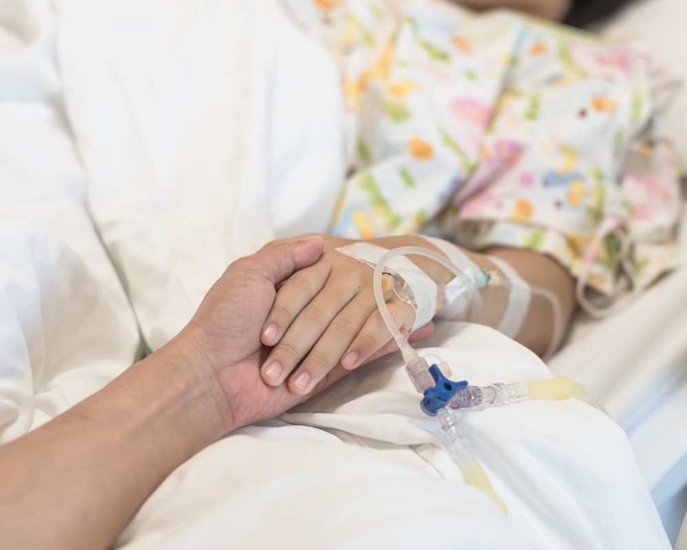 female in hospital bed, arm with an IV showing, a caregiver is holding her hand,