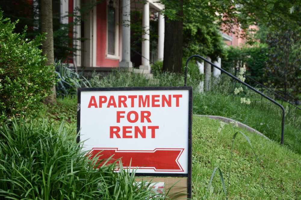apartment for rent sign (red letters on white background) in an green but overgrown yard in front of housing in NC town. Tenants must be given specific reasons for evictions, in this NC Supreme Court ruling.