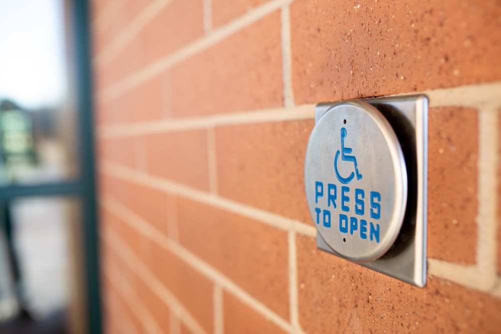Accessible Entrance, metal door button with a wheelchair symbol with the words "Press to open" on the side of a government building