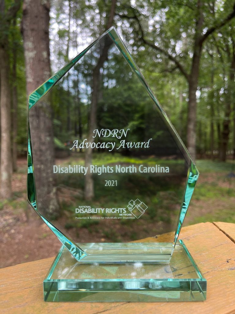 Glass NDRN Advocacy Award to Disability Rights NC in front of trees