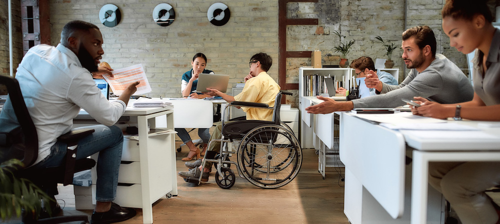 Young asian man with a disability shows a coworker something on his laptop