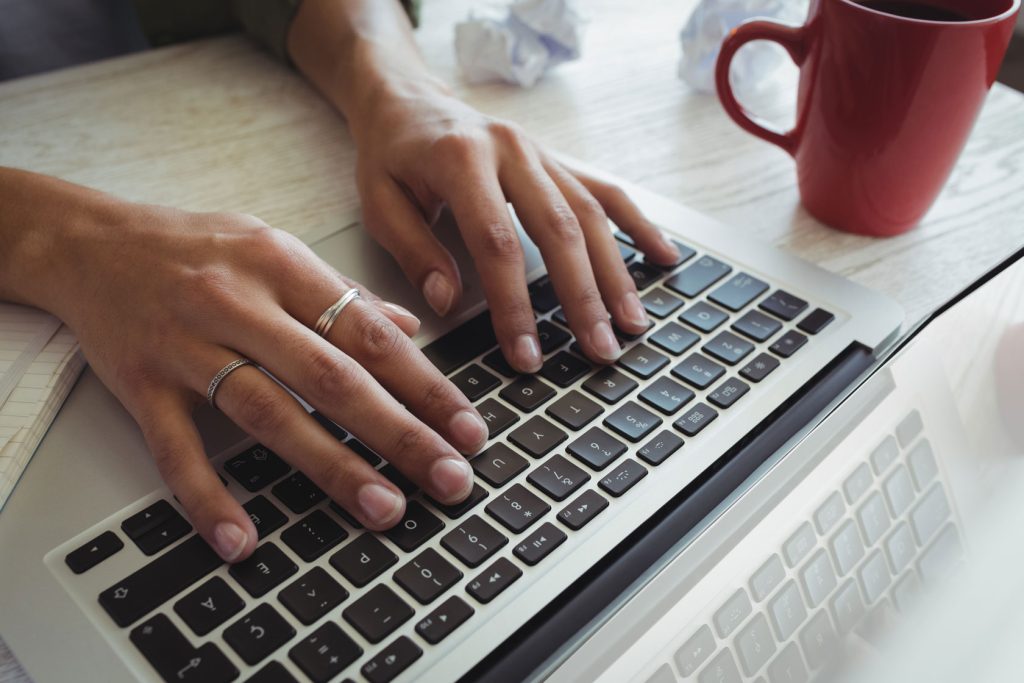 Latina woman types on laptop with red mug next to her hands