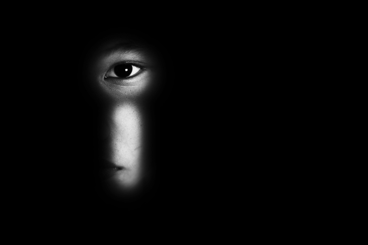 A child looks through a keyhole in the door of a prtf room. Only the eye and a sliver of the face is visible.
