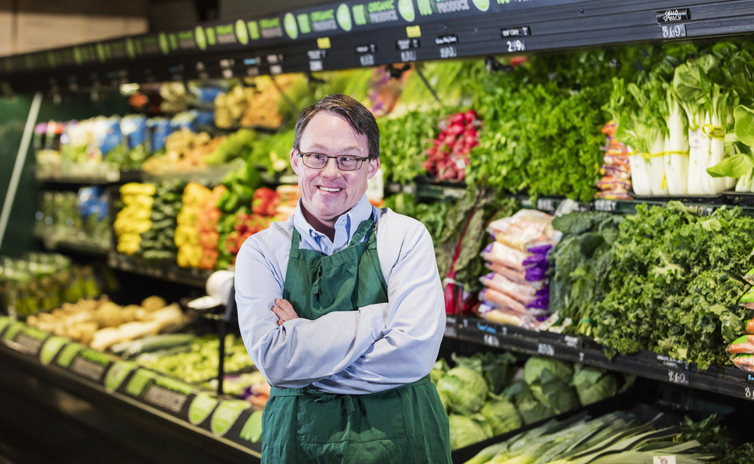a young man with glasses, brown hair and down syndrome wearing a grocery apron in a store where he works