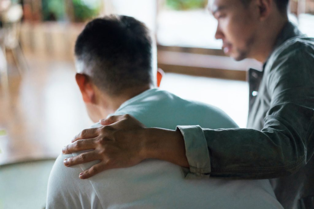 Rear view of son and elderly father sitting together at home.