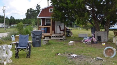 a small red storage shed with a wheelchair and garbage can outside the door