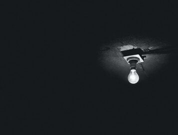 darkness with only a dim lightbulb visible on the ceiling, symbolizing the darkness, isolation and torture of solitary