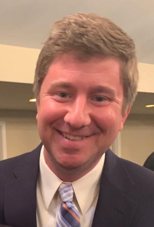 Headshot of Michael Shay, a white male 30 to 40 years old with brown hair, blue eyes, wearing a black suit with a white shirt and striped blue tie