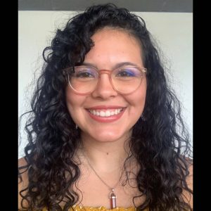 A headshot of a young woman with long curly brown hair and glasses.