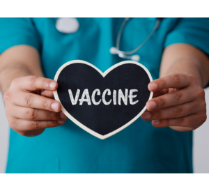 A nurse's hands holding a heart shaped sign that reads vaccine