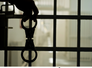 a person's hand behind the bars of a prison or jail, holding handcuffs