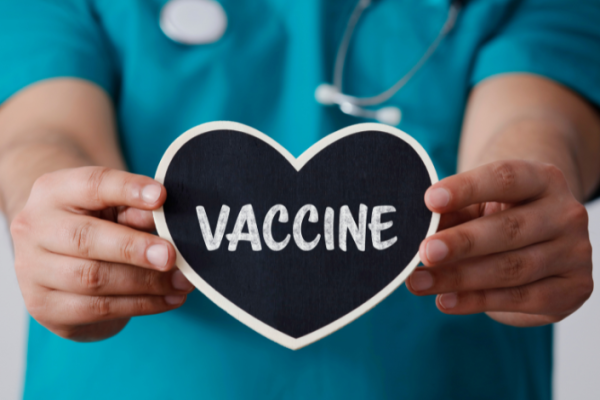 A nurse's hands holding a heart shaped sign that reads vaccine