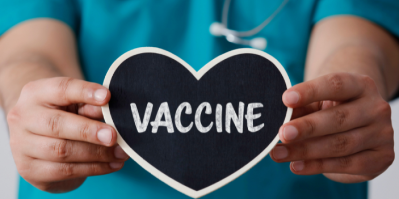 A nurse's hands holding a heart shaped sign that reads vaccine