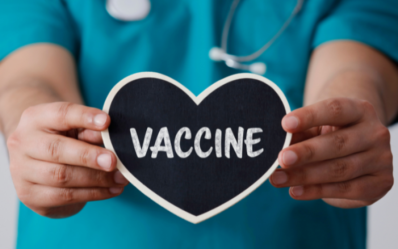 A nurse's hands holding a heart shaped sign that reads vaccine