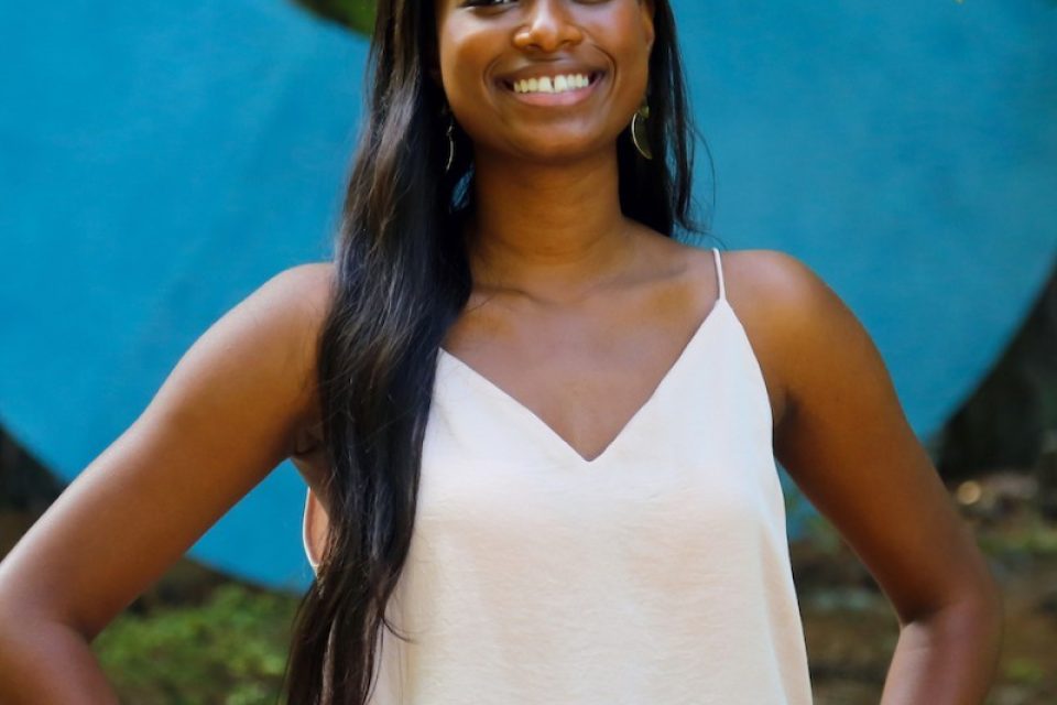 Picture of a woman in a white tank top smiling at the camera with her hands on her hips.
