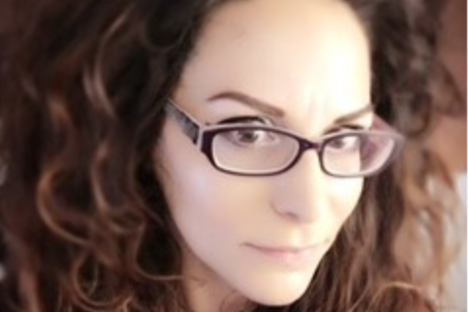 Close up a a woman with brown glasses and brown curly hair.