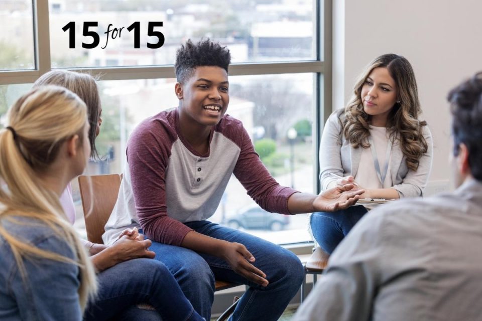 College aged male with dark skin sits in a circle with other students