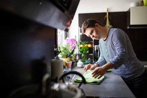 Adult man with down syndrome stands indoors in his kitchen at home