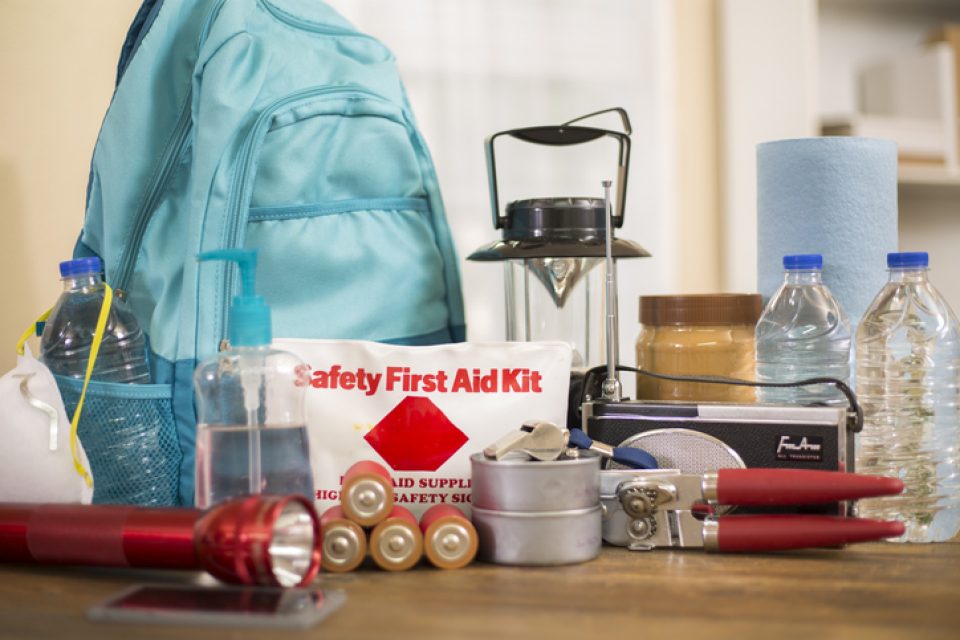 Emergency supplies gathered to create a kit, including a backpack, first aid kit, batteries, water and a mask.