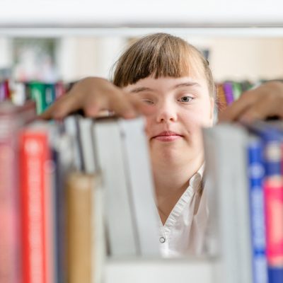 Girl with syndrome down chooses a book on a shelf in the library