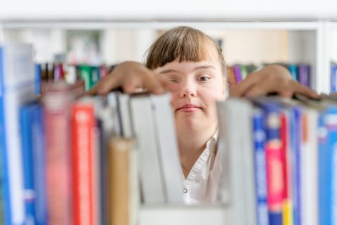 Girl with syndrome down chooses a book on a shelf in the library