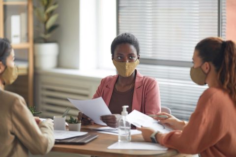 A group of diverse women sitting around a table in a school building, all wearing masks during a IEP meeting.