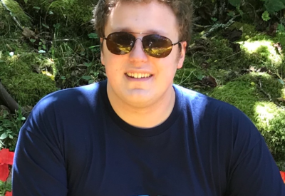 Kellen Kellen smiling at the camera on a sunny day, wearing sunglasses and a dark blue Myrtle Beach t-shirt.