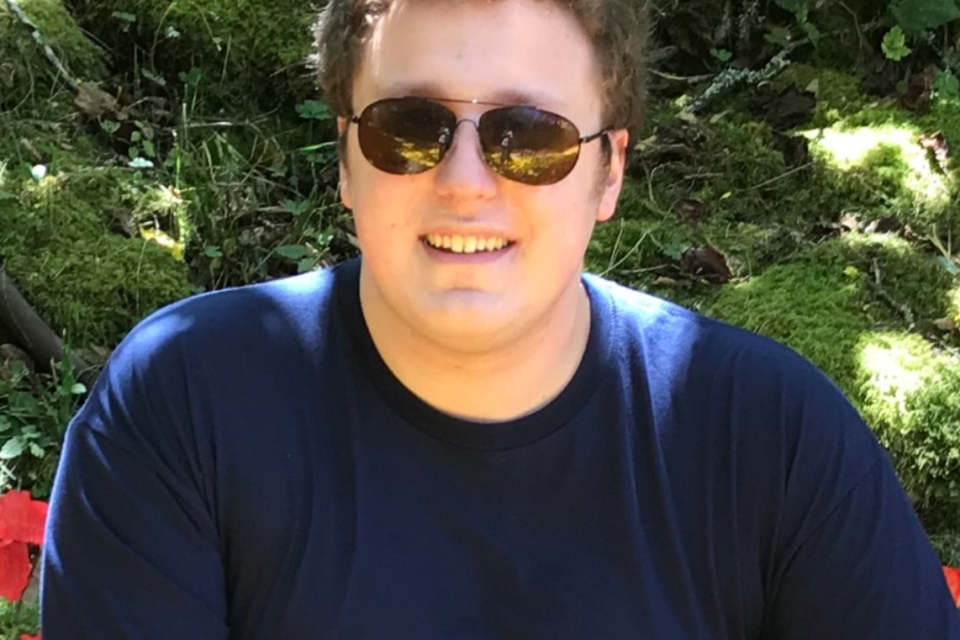 Kellen smiling at the camera on a sunny day, wearing sunglasses and a dark blue Myrtle Beach t-shirt.