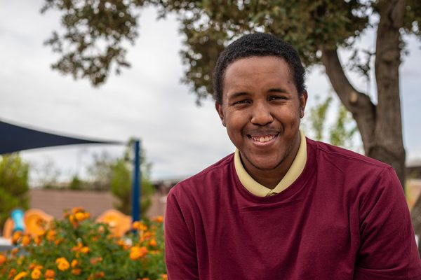 Man-next-to-flowers Black man with I/DD sits in front of flowers in a community garden