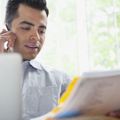 Man using phone while reading paperwork