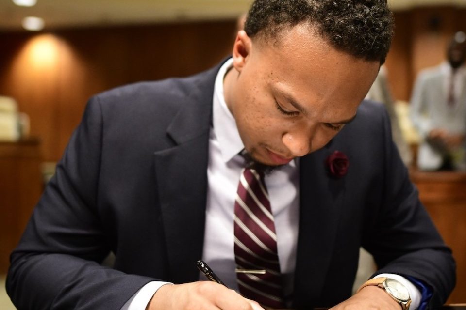 Young Black man in suit sitting at a table signing a paper