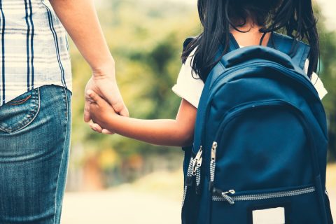 Child wearing backpack holds parent's hand