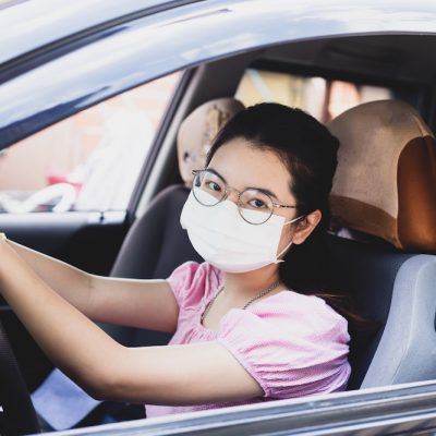 asian woman wearing glasses, pink shirt and a white mask driving a lyft.