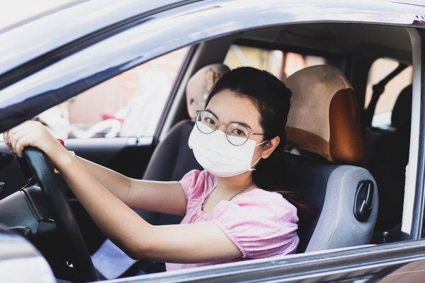 asian woman wearing glasses, pink shirt and a white mask driving a lyft.