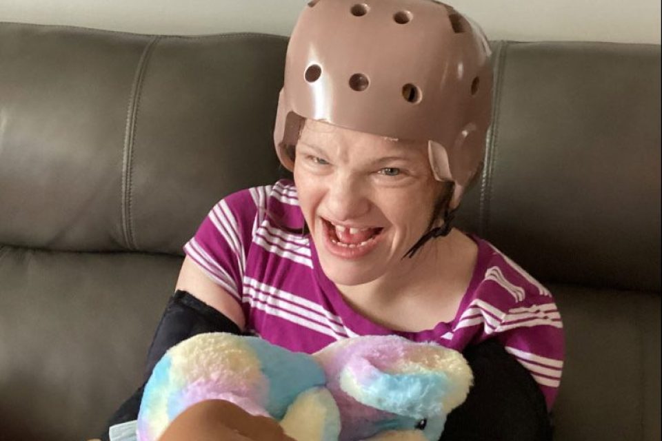 A picture of a young woman wearing a helmet and smiling while sitting on a couch