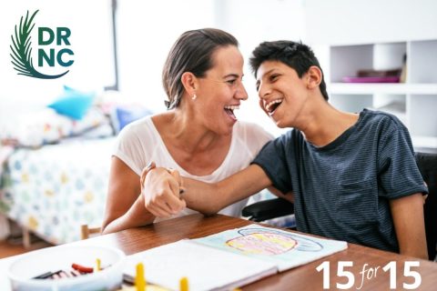 teenage boy with a disability laughing with a female caretaker while coloring at the table