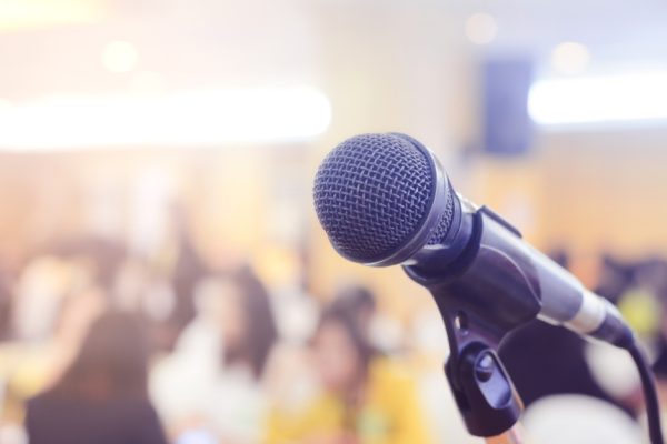 Microphone in focus, with a conference room full of people blurred in the background