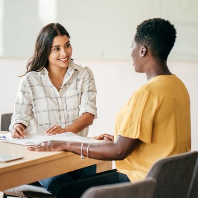 Two women are sitting at a table, smiling and talking, while completing paperwork