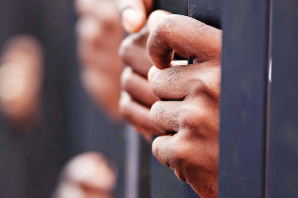 The hands of several prisoners gripping bars of their cell