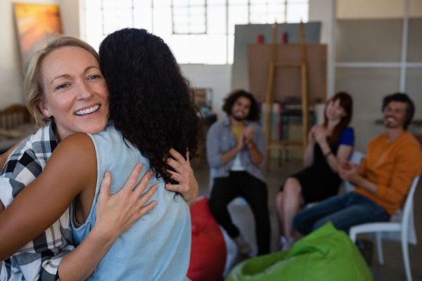 Two woman hug as friends clap from chairs
