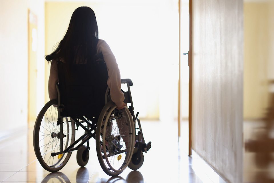 Woman in wheelchair in dark hallway looks out window