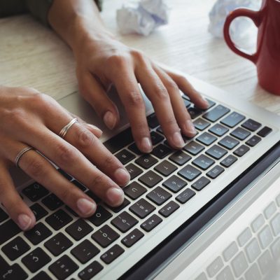 Latina woman types on laptop with red mug next to her hands