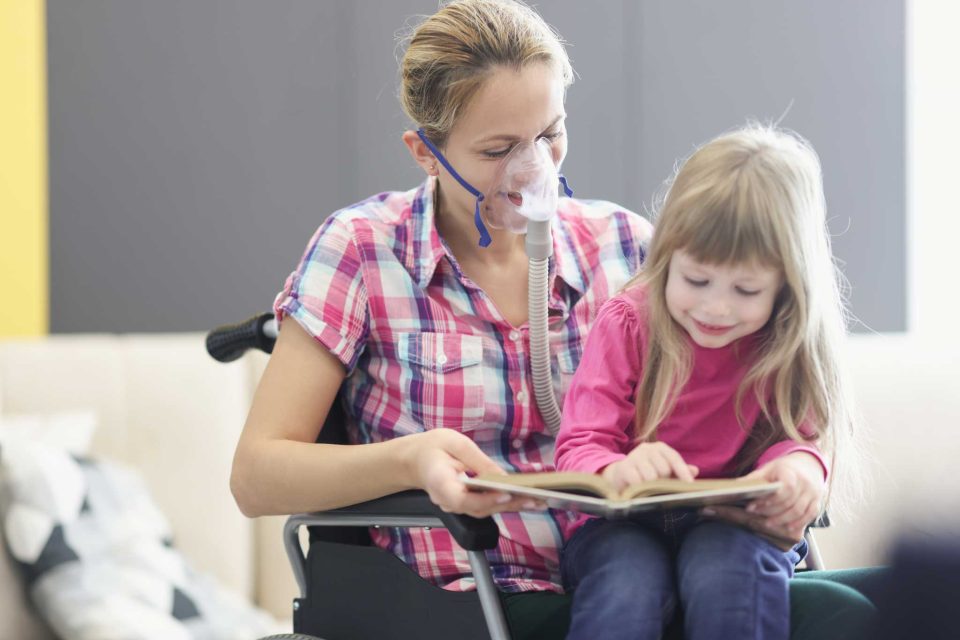 Woman in wheelchair with oxygen supply holds young girl