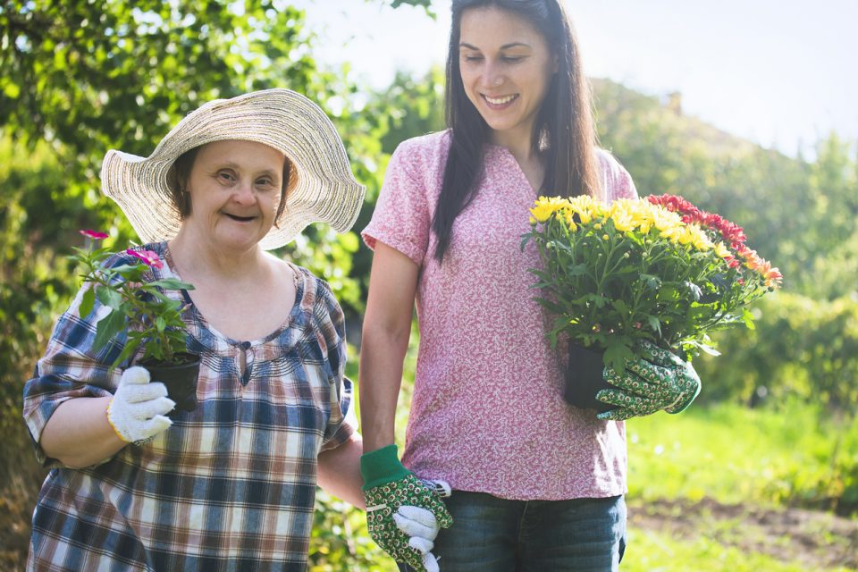 Woman with Down Syndrome and her relative planting flowers together. Gardening.