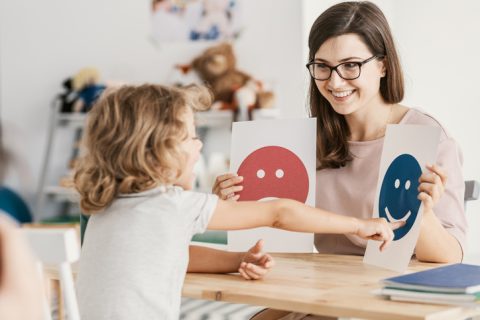 child with autism identifies emotions using cards held up by psychologist during play therapy