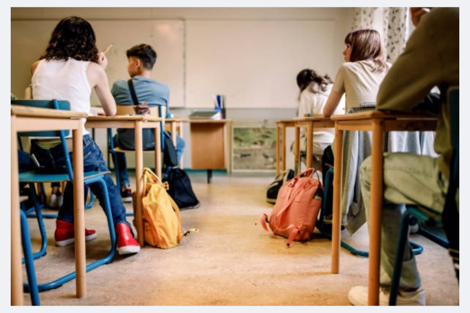 a group of 5 students in a classroom sitting at desks facing away from the camera